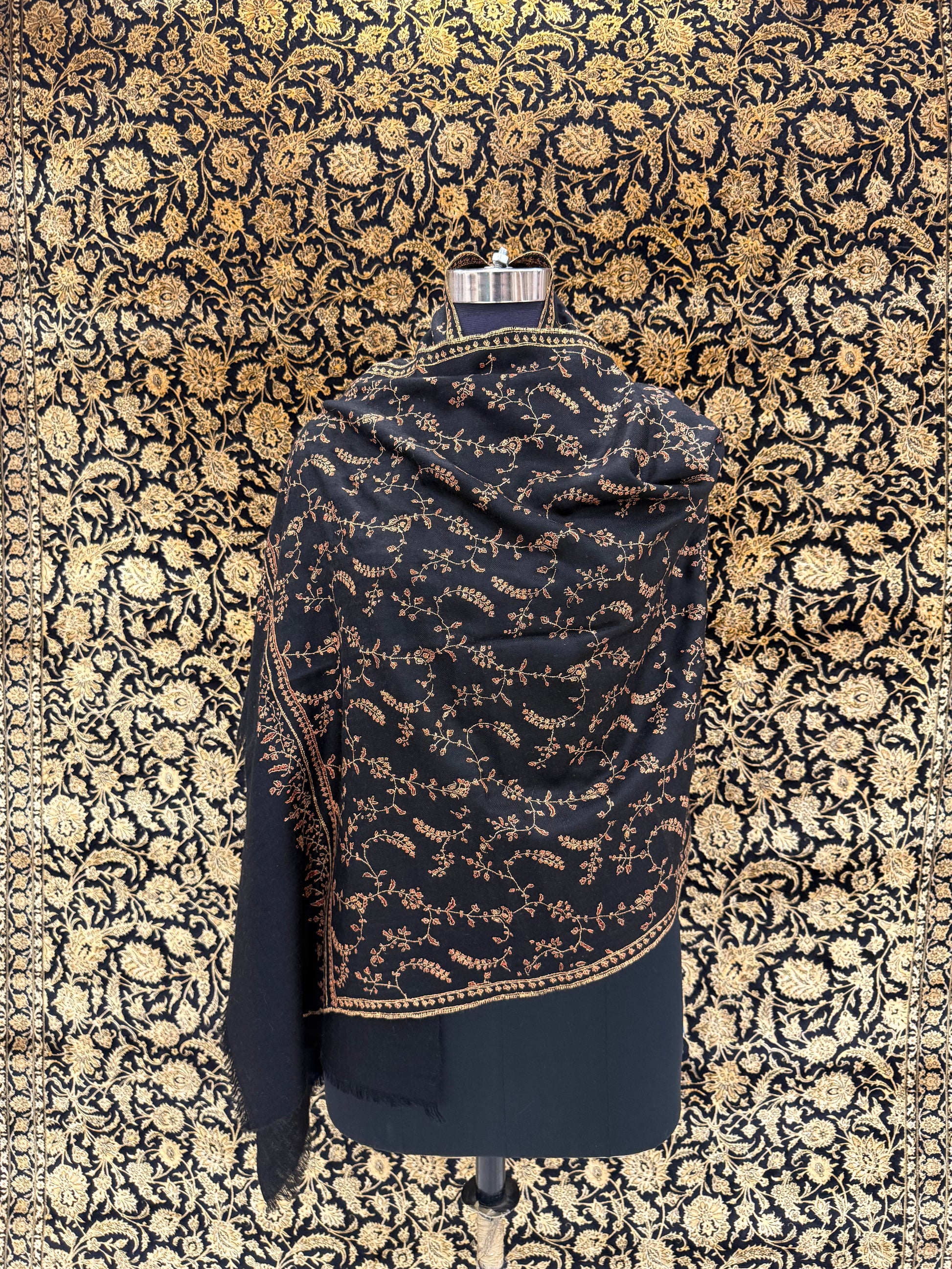 Black and gold patterned fabric on a mannequin against a floral patterned wall.